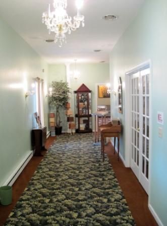 Long hallway with patterned runner rug, glass doors, chandelier, and small tables in a bright interior