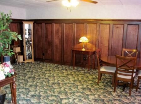 Wood-paneled room with patterned carpet, lamp, and wooden chairs beside a small table