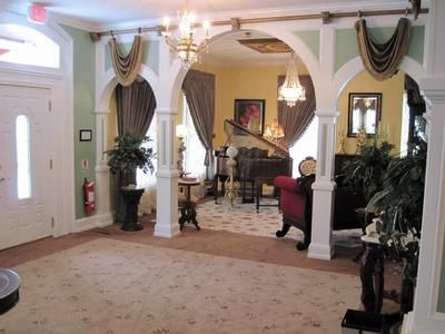 Elegant foyer with white arches, draped curtains, chandelier, piano, and patterned carpet