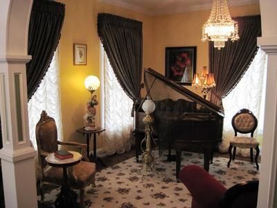 Elegant living room with a grand piano, chandelier, dark curtains, and floral carpet.