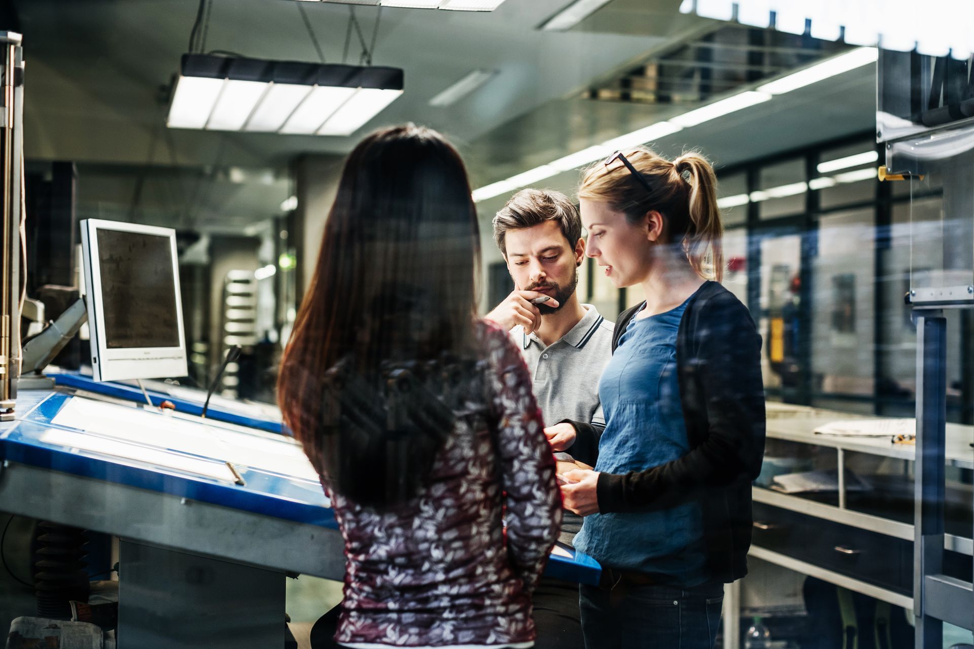 Three colleagues discussing a project near a blue workstation in an office.