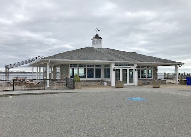 Small waterfront pavilion with stone columns and benches under a gray overcast sky