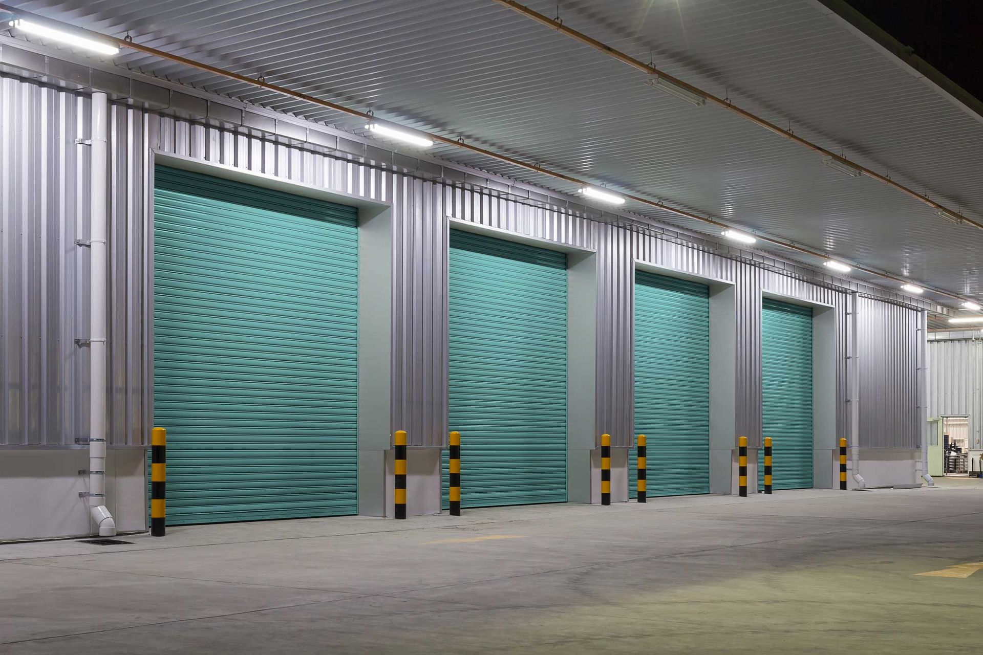 A row of green garage doors in a warehouse at night.