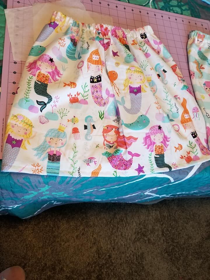 A mermaid-patterned fabric skirt with an elastic waistband resting on a pink cutting mat.