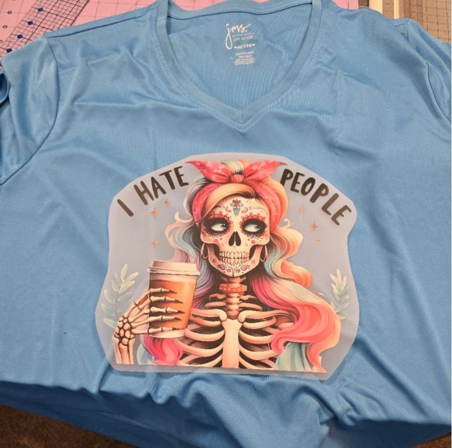 Light blue V-neck t-shirt featuring a sugar skull graphic with colorful hair holding a coffee cup, captioned 