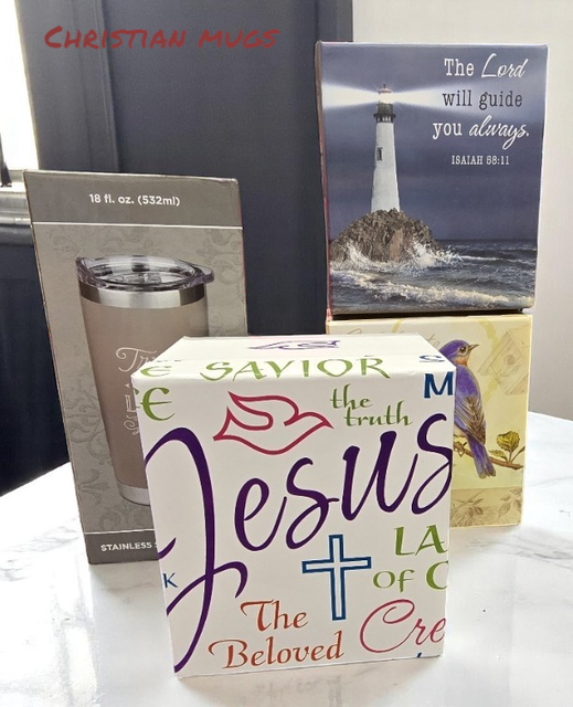 A Christian tumbler in a box, a lighthouse box with scripture, and a box with Jesus-themed text on a white table.