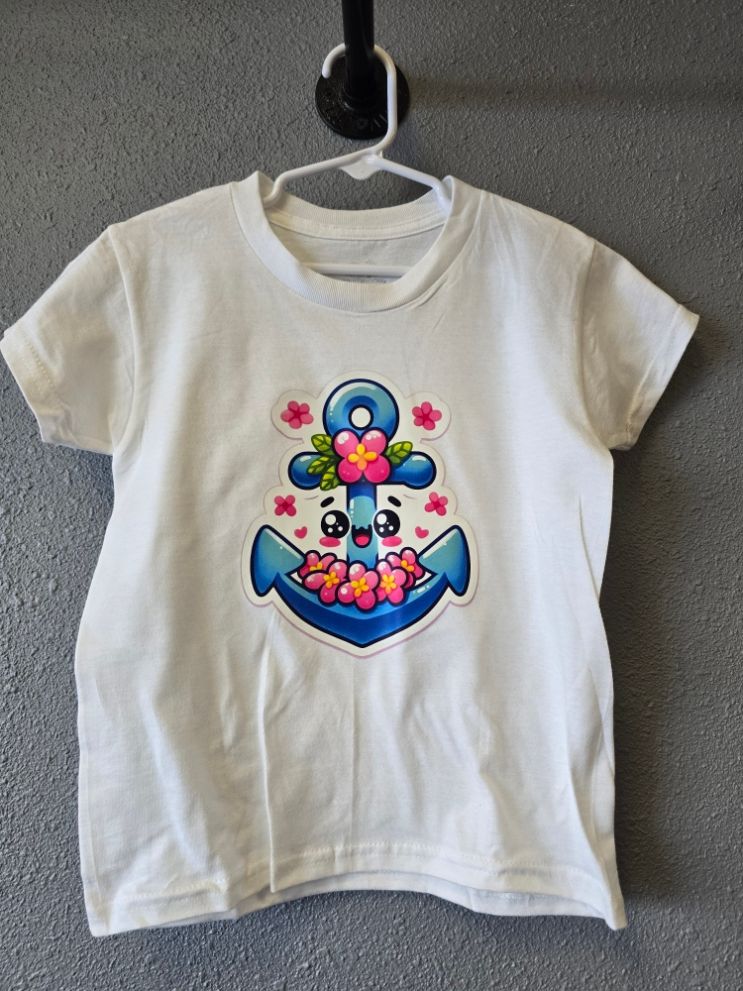 A white t-shirt hanging on a hook, featuring a cartoon blue anchor with a happy face surrounded by pink flowers.