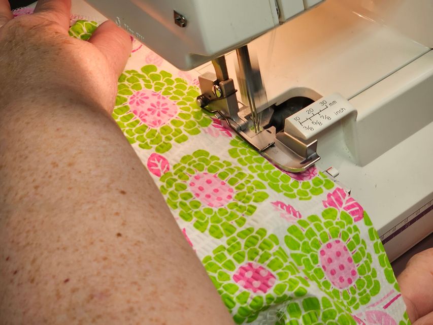 A person uses a sewing machine with a special foot attachment to stitch a fabric featuring a green and pink floral pattern.