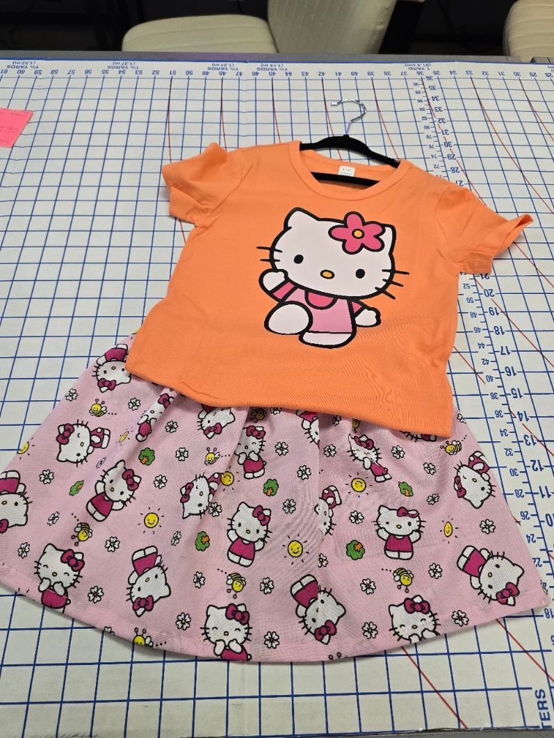 An orange Hello Kitty t-shirt paired with a pink Hello Kitty print skirt on a gridded cutting mat.