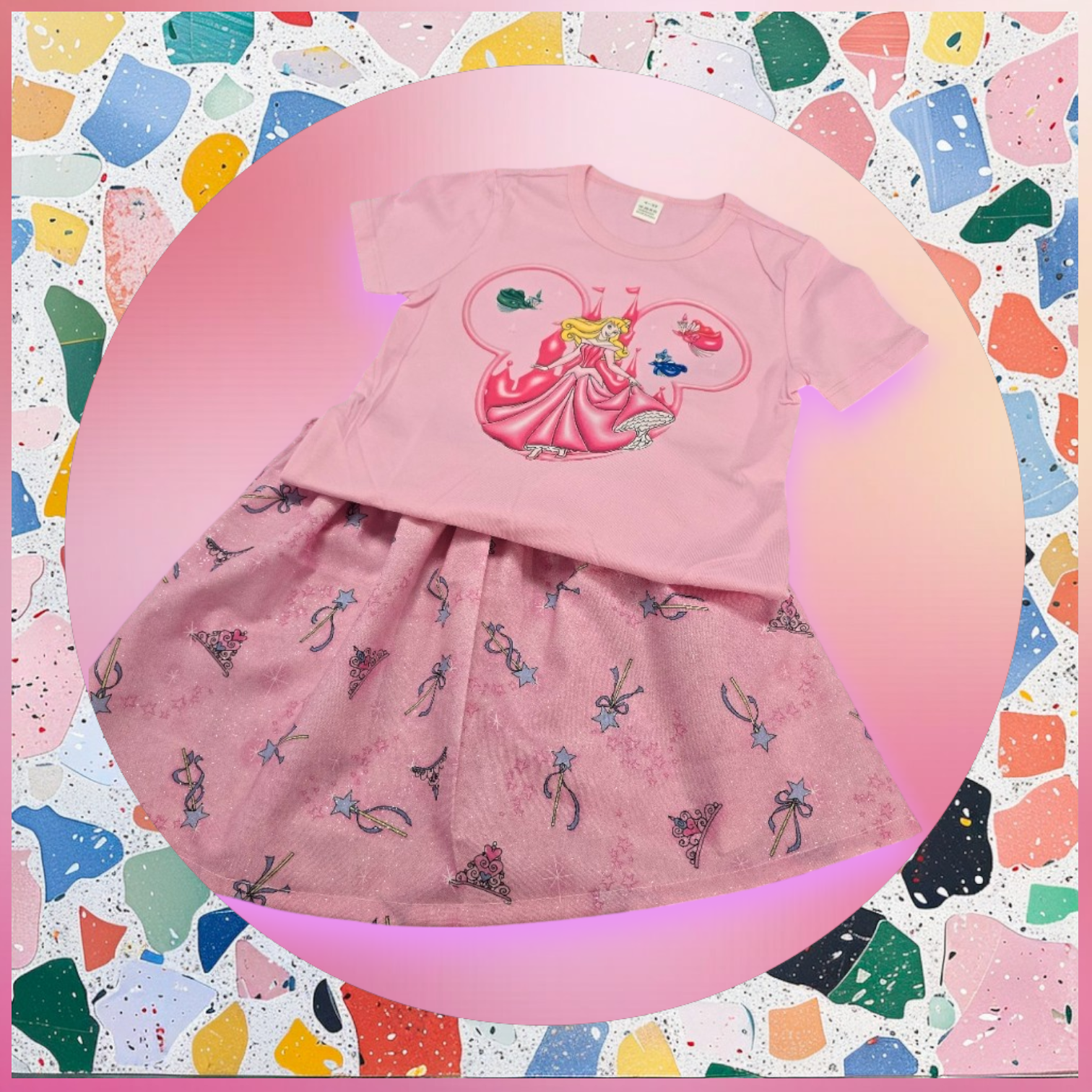 A pink child's t-shirt and skirt set featuring a Disney princess graphic, set against a colorful terrazzo background.