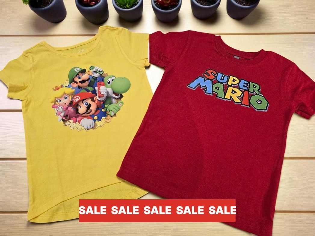 A yellow Super Mario t-shirt next to a red Super Mario logo t-shirt on a wooden surface with a red sale banner overlay.