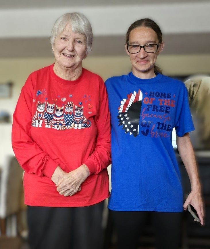 Two people standing side-by-side, wearing a red shirt with patriotic cat illustrations and a blue patriotic-themed t-shirt.