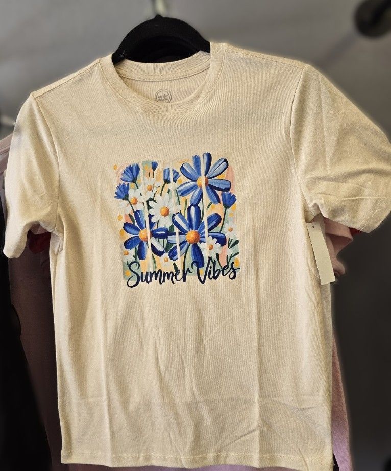 A cream-colored T-shirt on a hanger, featuring blue daisies and the text 