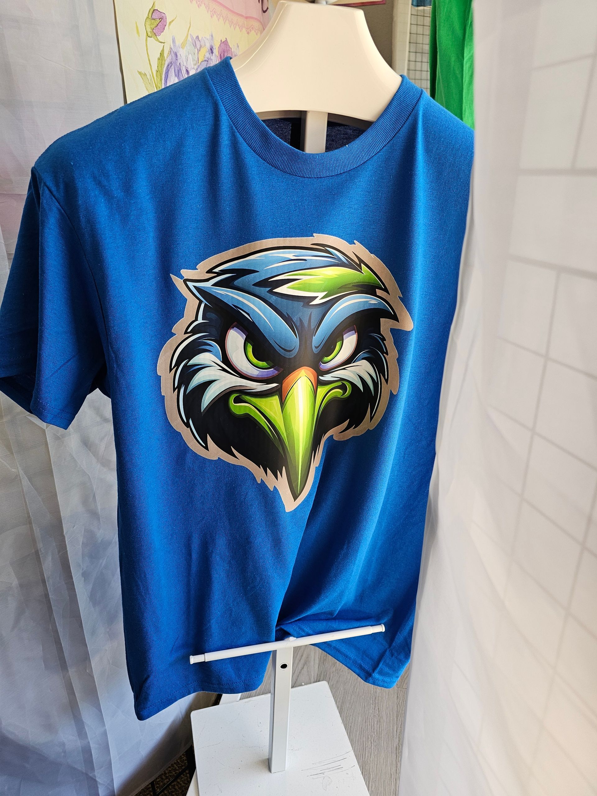 A blue heathered t-shirt on a mannequin display, featuring a graphic of an aggressive-looking bird with a bright green beak.