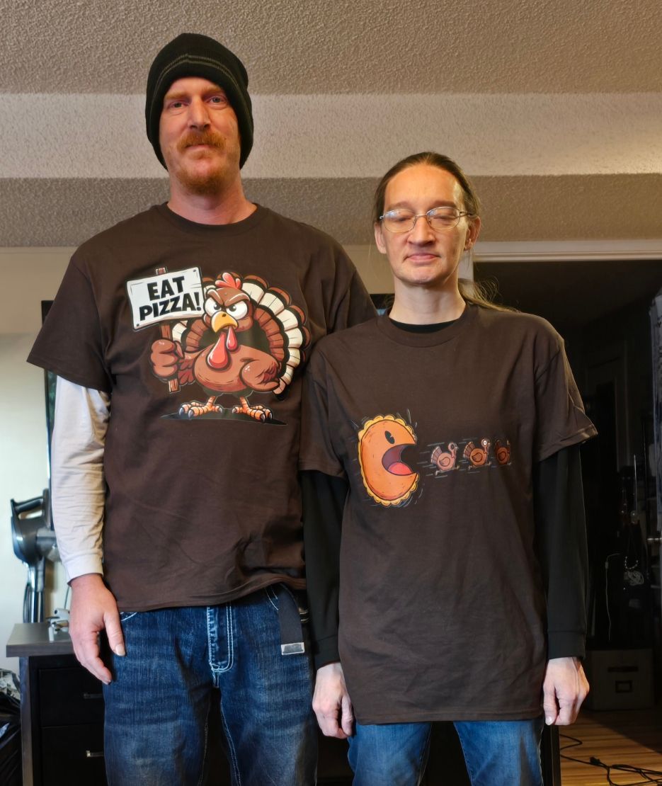 Two people standing indoors wearing brown t-shirts with Thanksgiving-themed graphics.
