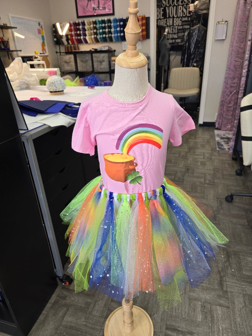 Pink T-shirt with a rainbow and pot of gold design, paired with a multi-colored sparkly tutu on a mannequin.