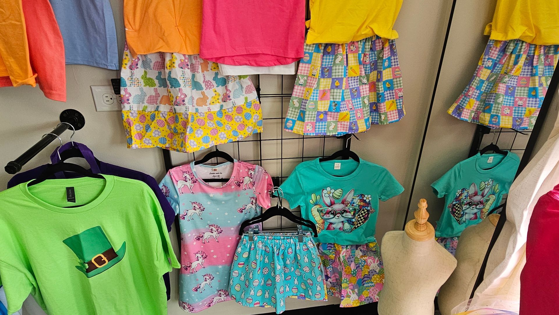 Clothing display featuring bright, colorful t-shirts and matching patterned skirts or shorts on racks and a mannequin.