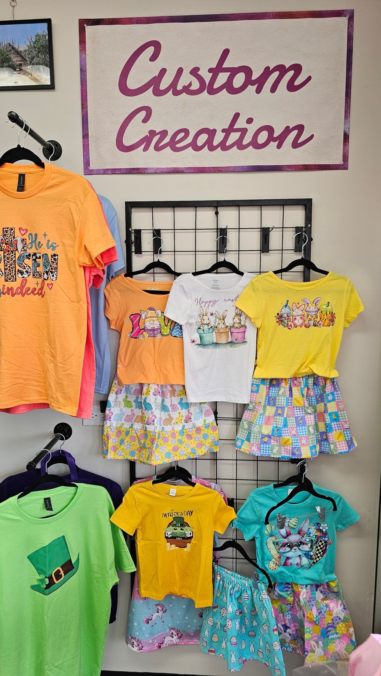A store display featuring colorful custom t-shirts and matching skirts hanging on racks under a 