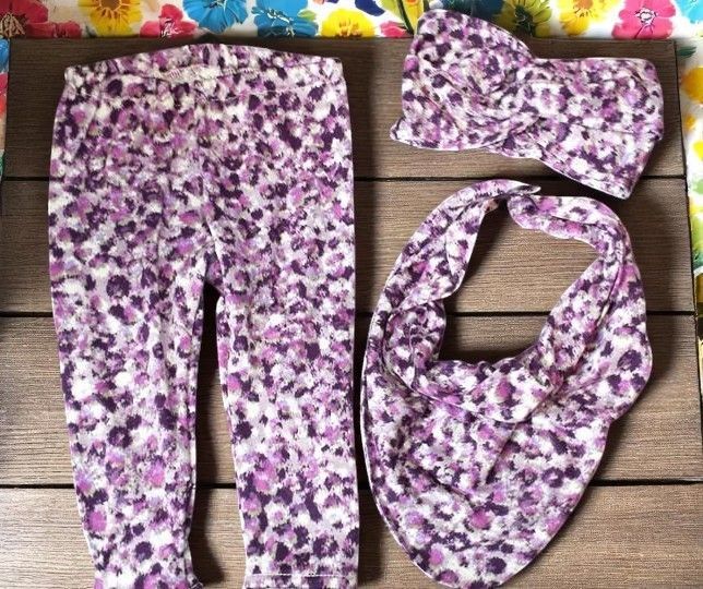 A matching three-piece baby clothing set featuring purple and white leopard print leggings, a headband, and a bib.