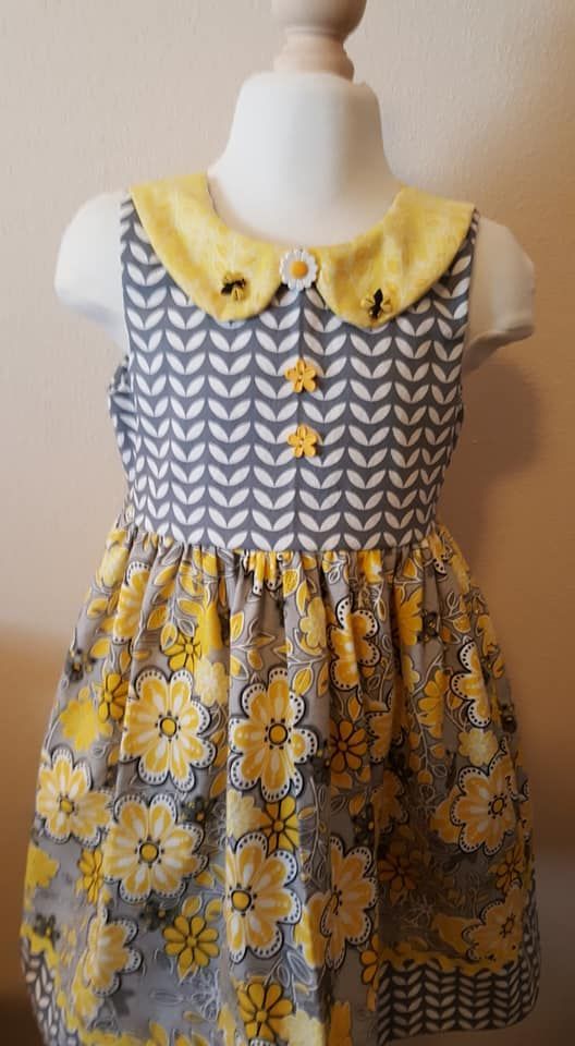 A sleeveless dress with a grey and white chevron bodice, a yellow collar with bee accents, and a yellow floral skirt.