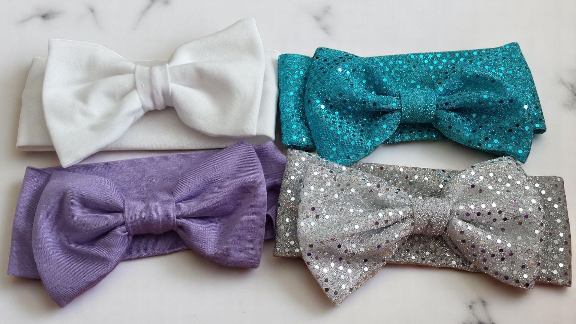 Four baby headbands with bows, arranged in a grid, in white, turquoise glitter, light purple, and silver glitter colors.