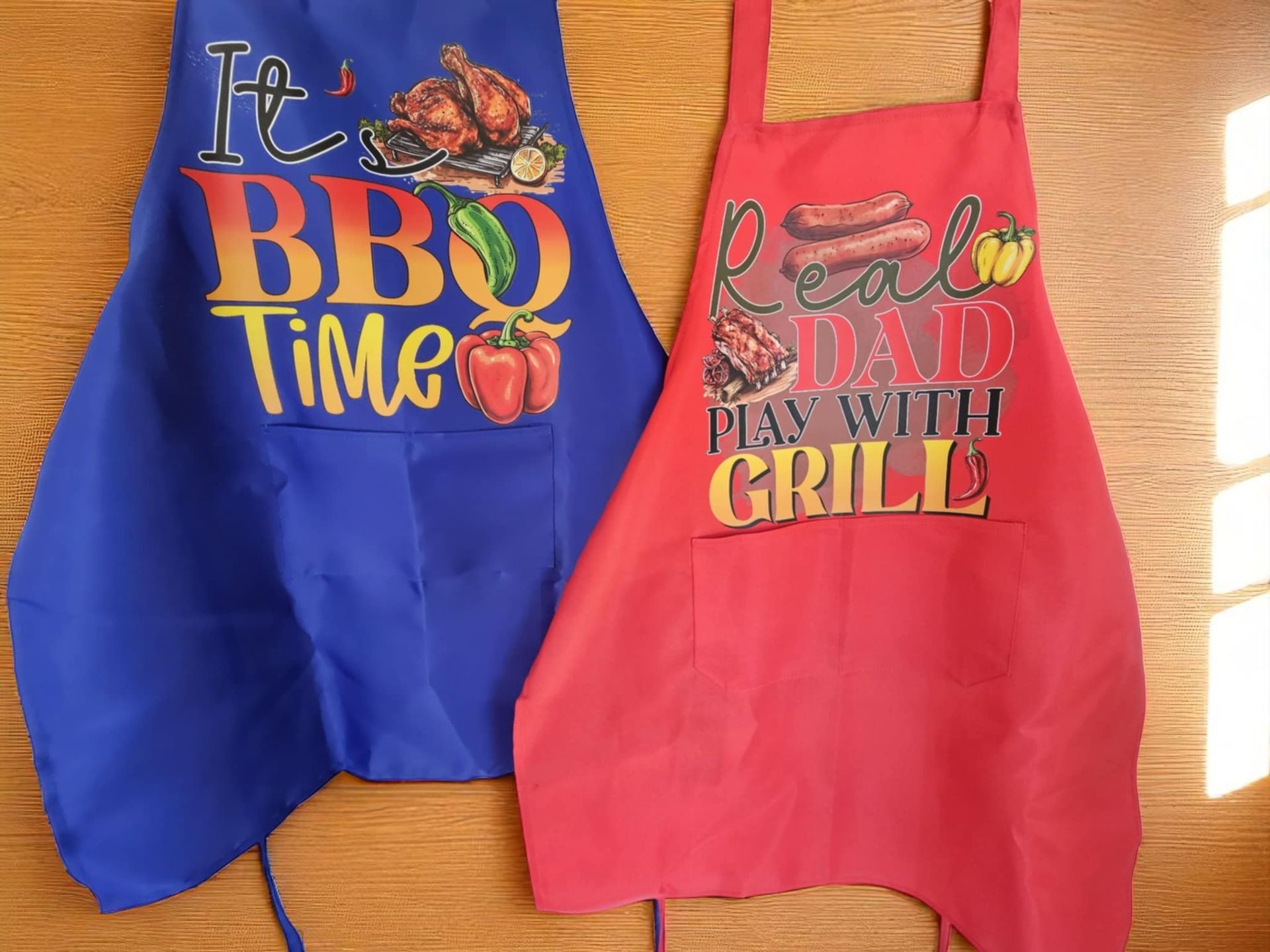 Two aprons side by side on a wooden surface: one blue saying 