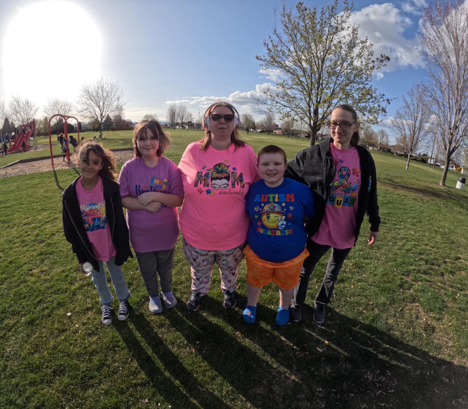 Five people standing together in a sunny park; they wear shirts with autism awareness themes.
