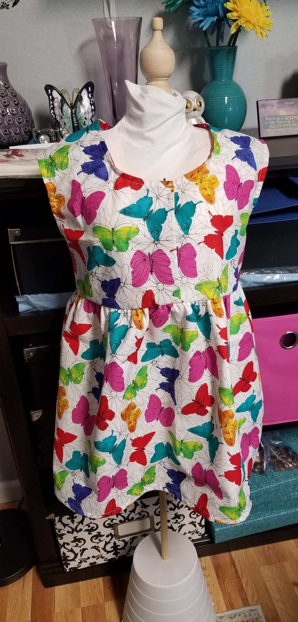 A dress with a colorful butterfly pattern on a white background, displayed on a mannequin in a room.