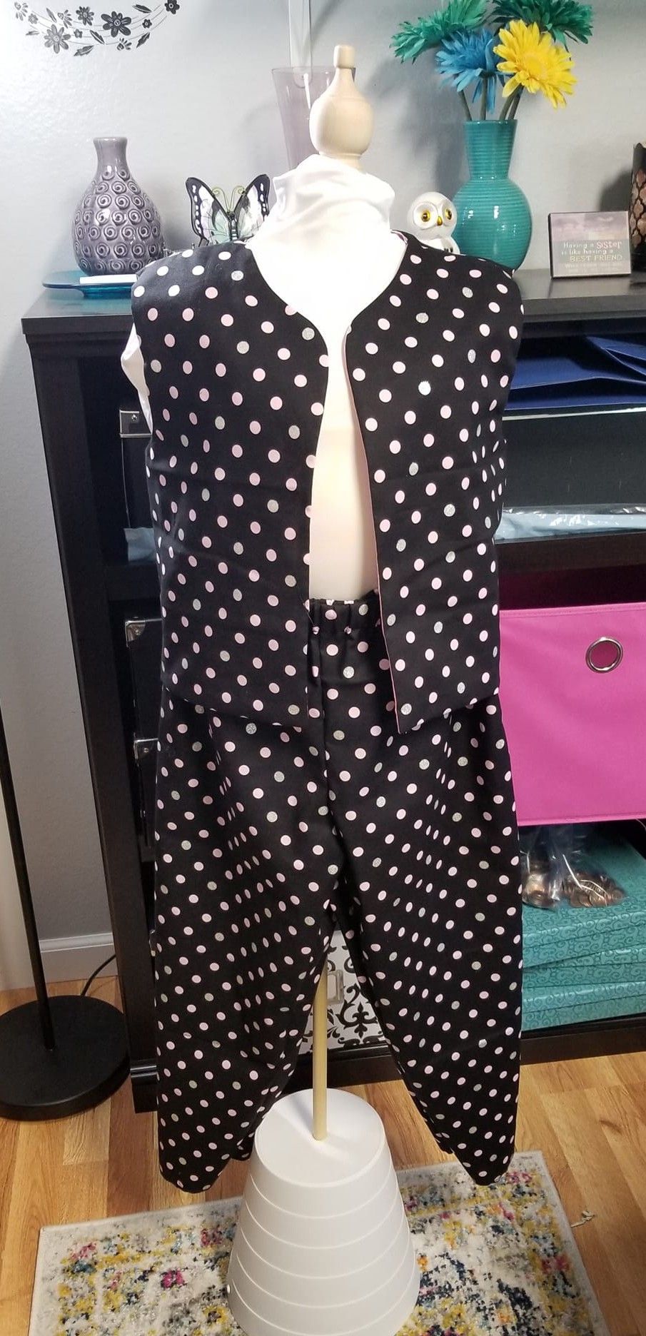 A black and white polka-dot vest and matching pants set displayed on a mannequin in a room.