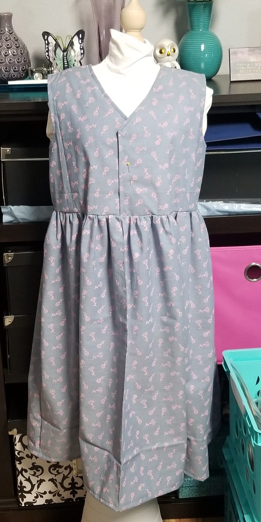 A light gray, V-neck dress with a small white floral pattern and a gathered waist displayed on a mannequin.