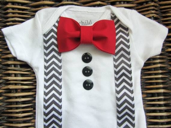 White baby onesie with a red fabric bow tie, three black buttons, and grey chevron print suspenders.