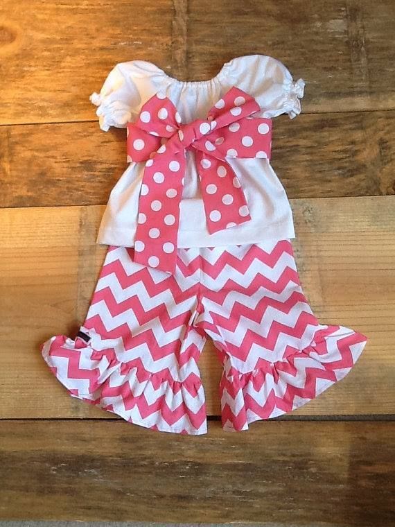 A white, short-sleeved top with a large pink and white polka-dot bow, paired with pink and white chevron-patterned ruffles.