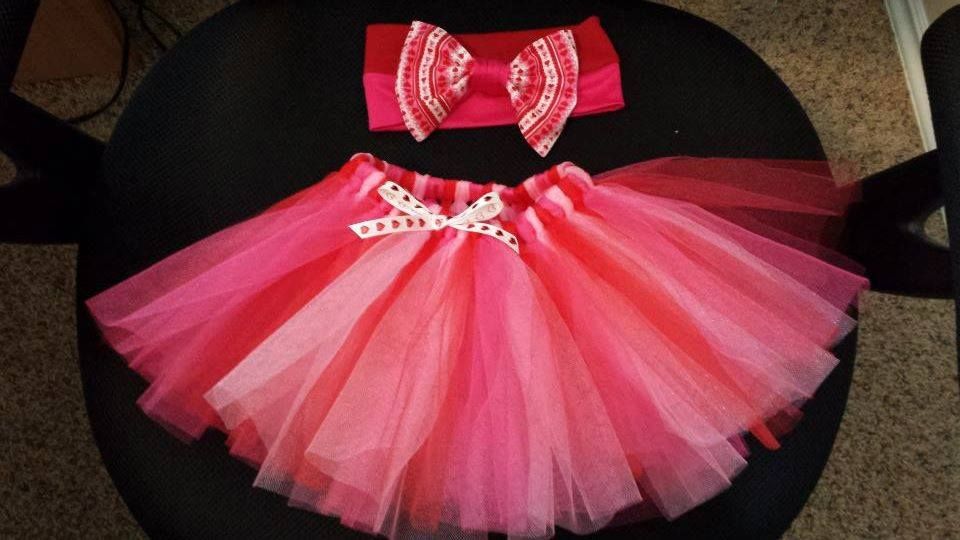 A pink and red tulle tutu with a matching headband featuring a bow, displayed on a black surface.