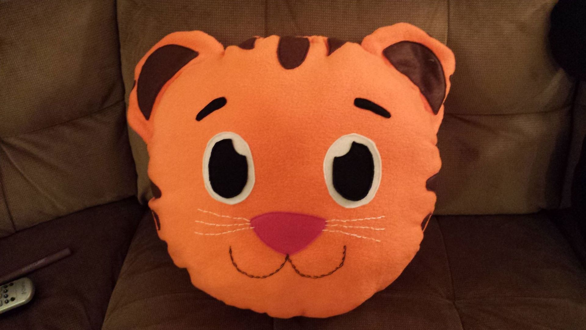 A plush pillow shaped like the head of Daniel Tiger, featuring bright orange fur, brown stripes, and a pink nose.