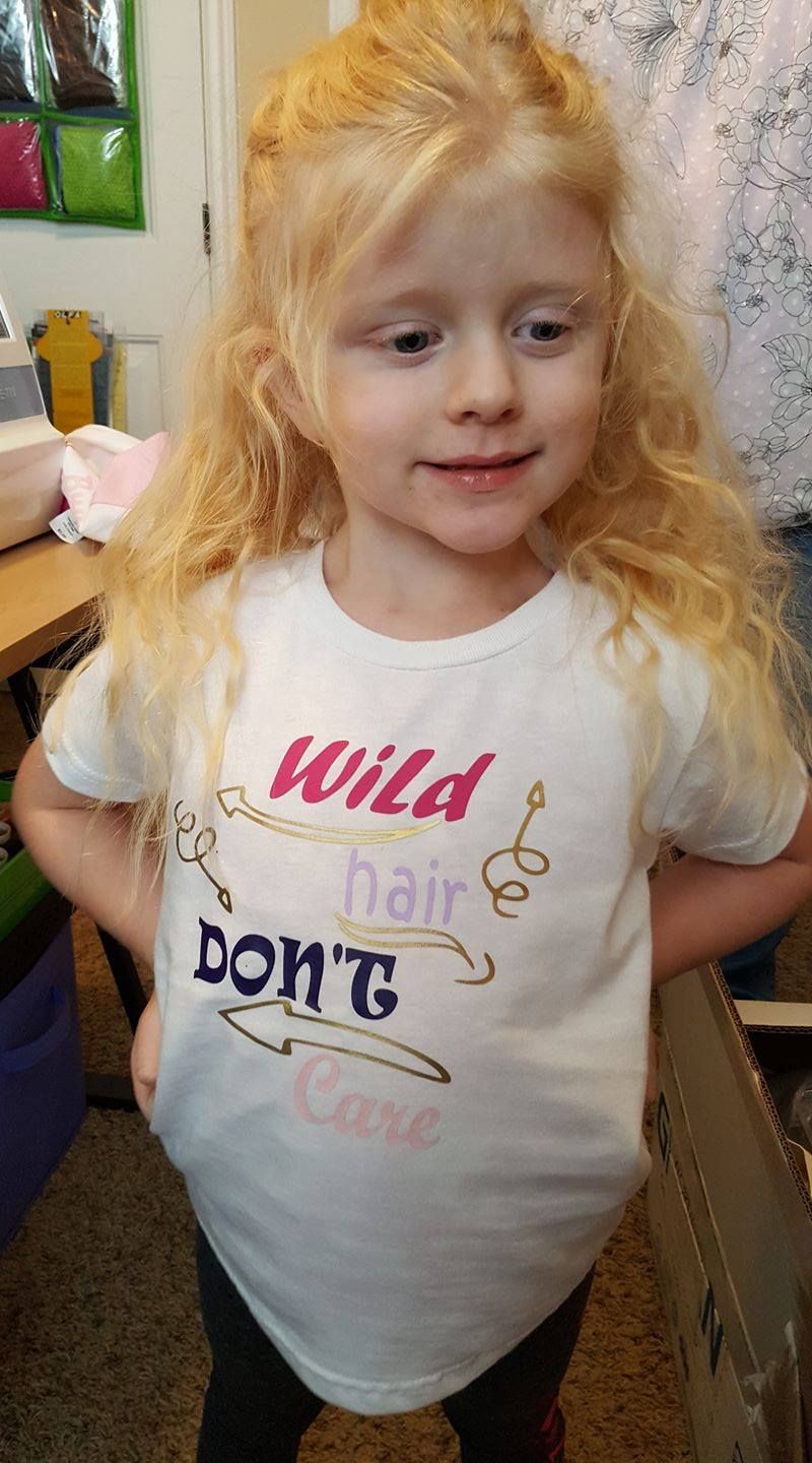 A child smiling and wearing a white t-shirt that says 