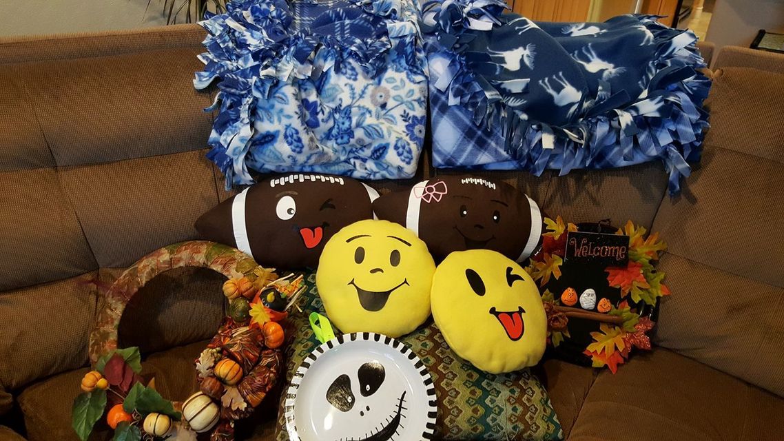 Two blue fleece blankets, two football pillows, two emoji pillows, and two autumn-themed wreaths on a brown sofa.