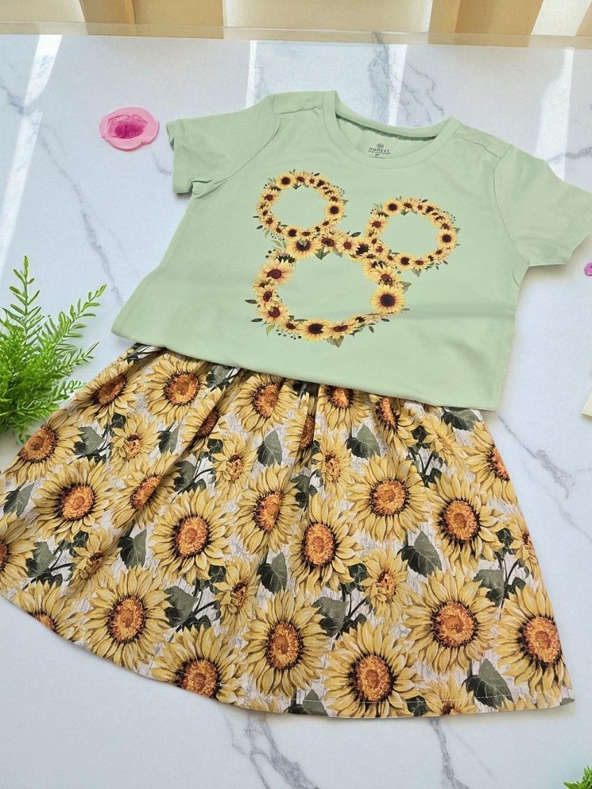 A light green t-shirt with a sunflower Mickey Mouse icon graphic, paired with a yellow sunflower-patterned skirt.