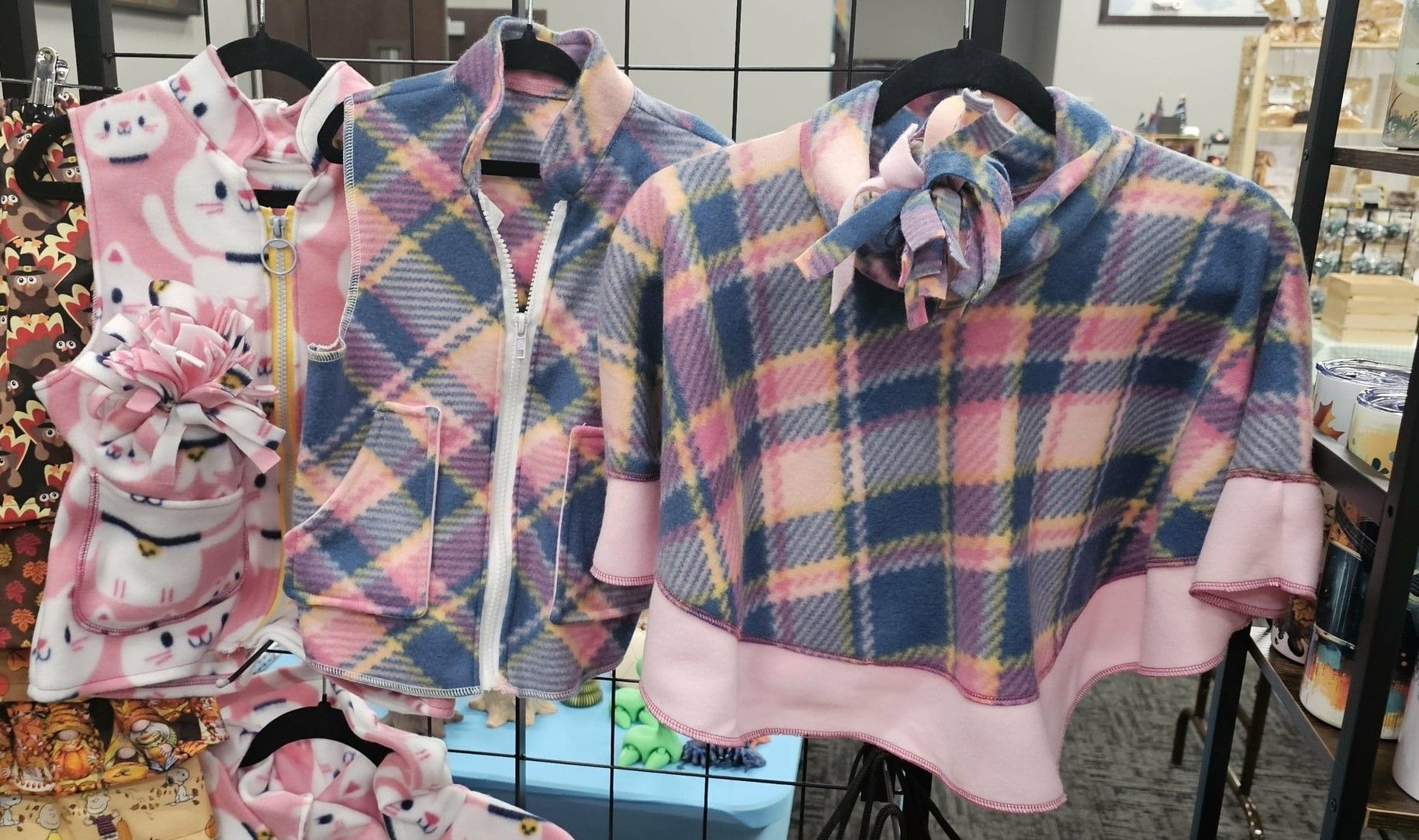 A display rack holding pink and blue plaid clothing items, including a zip-up vest and a turtleneck poncho.