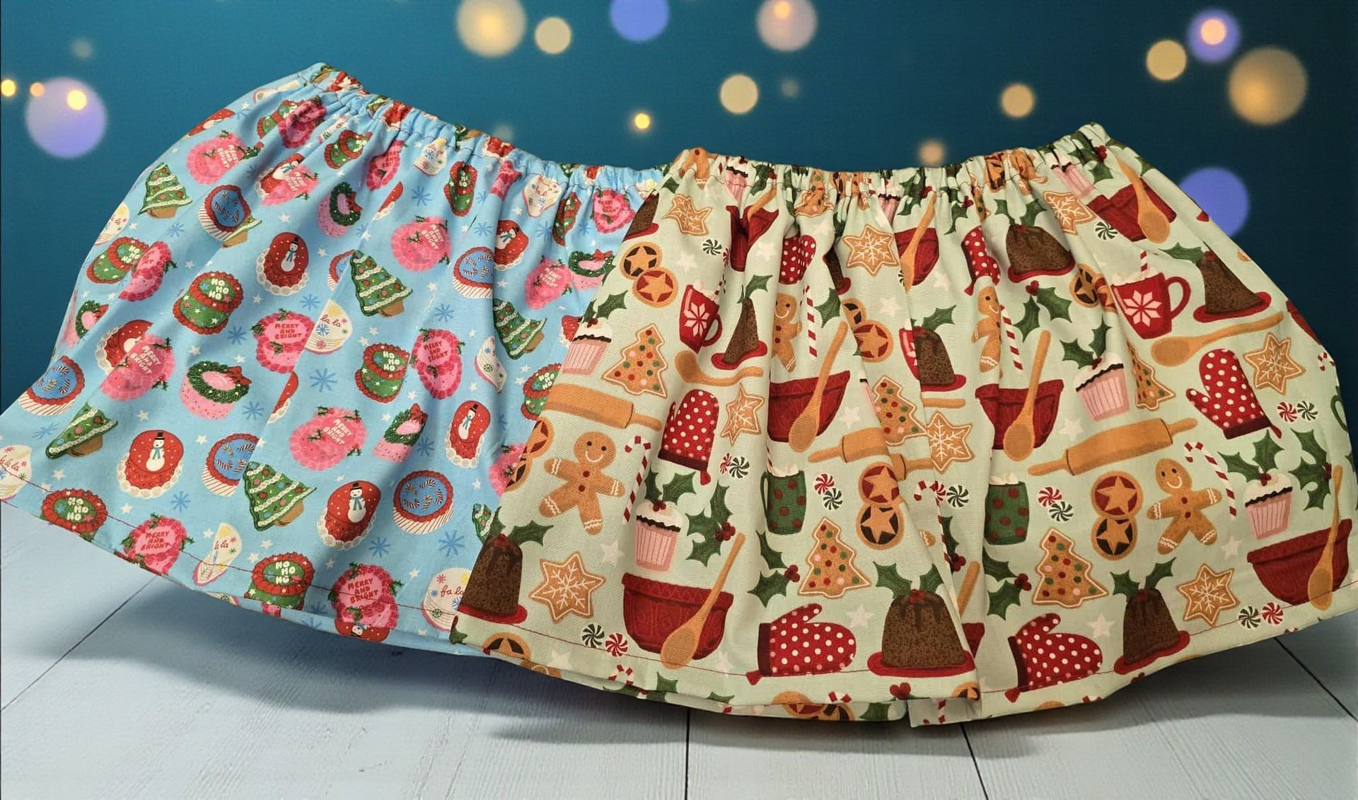 Two gathered fabric skirts with Christmas-themed patterns in blue and cream colors, displayed on a white surface.