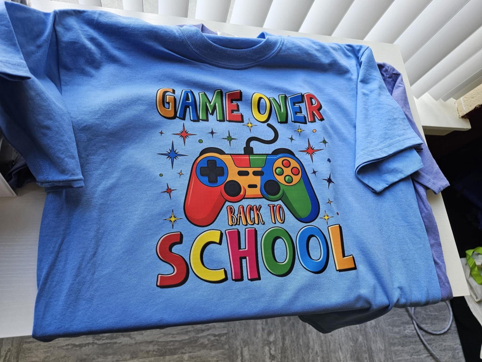 A light blue t-shirt with a colorful video game controller graphic and the text 