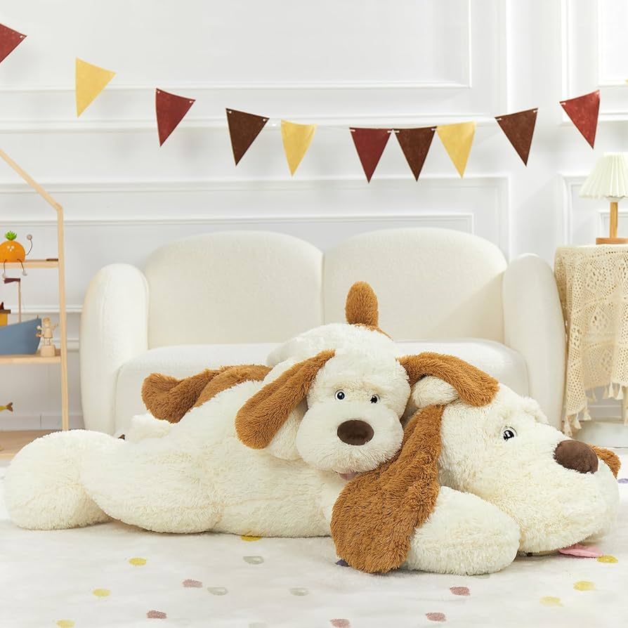 A large, cream and brown plush dog toy resting on a white floor in front of a white sofa and festive bunting.