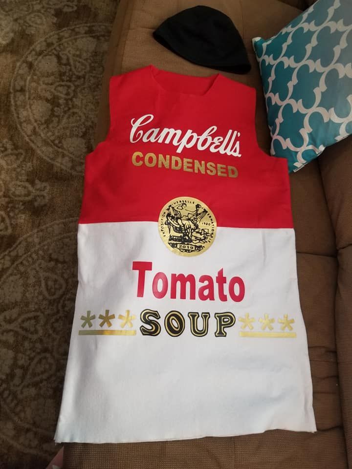 A sleeveless red and white dress designed to look like a can of Campbell’s Tomato Soup, with a black hat nearby.