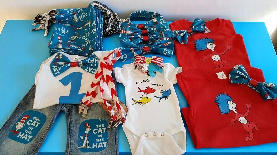 Dr. Seuss-themed baby and child clothing set including t-shirts, onesies, patterned bow ties, and pants on a blue table.
