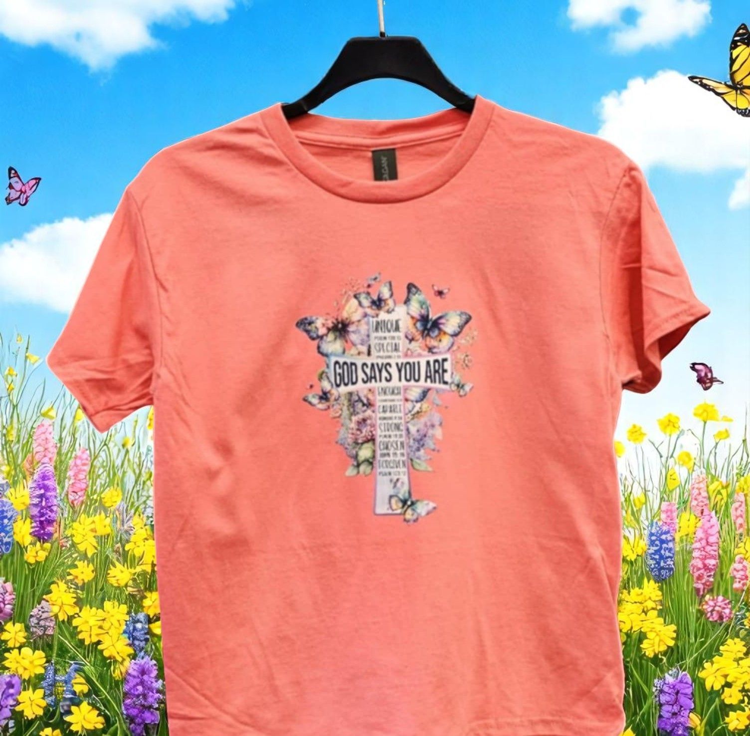 A coral t-shirt with a graphic cross design featuring butterflies and the text 
