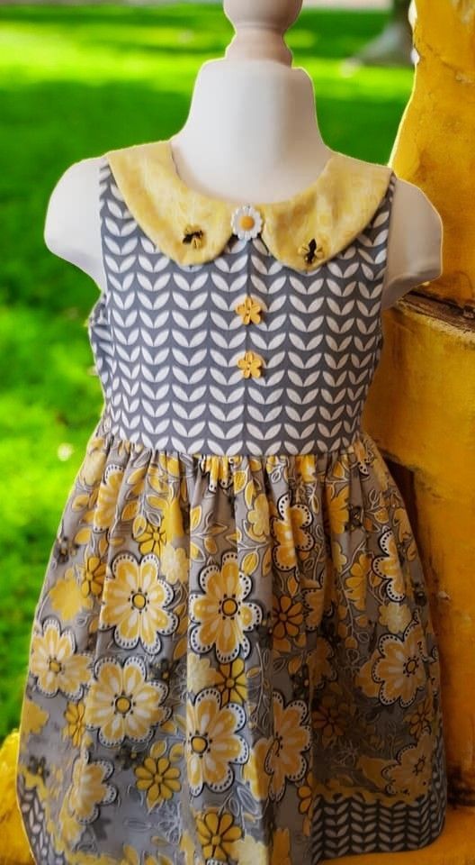 A dress on a mannequin with a yellow collar with small bee motifs, a gray chevron bodice, and a yellow floral skirt.