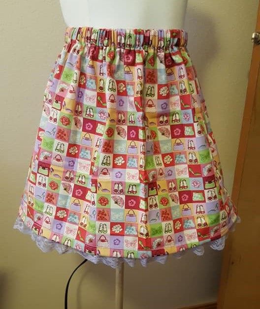 A colorful, patterned, elastic-waist skirt with a ruffled lace trim, displayed on a mannequin torso.