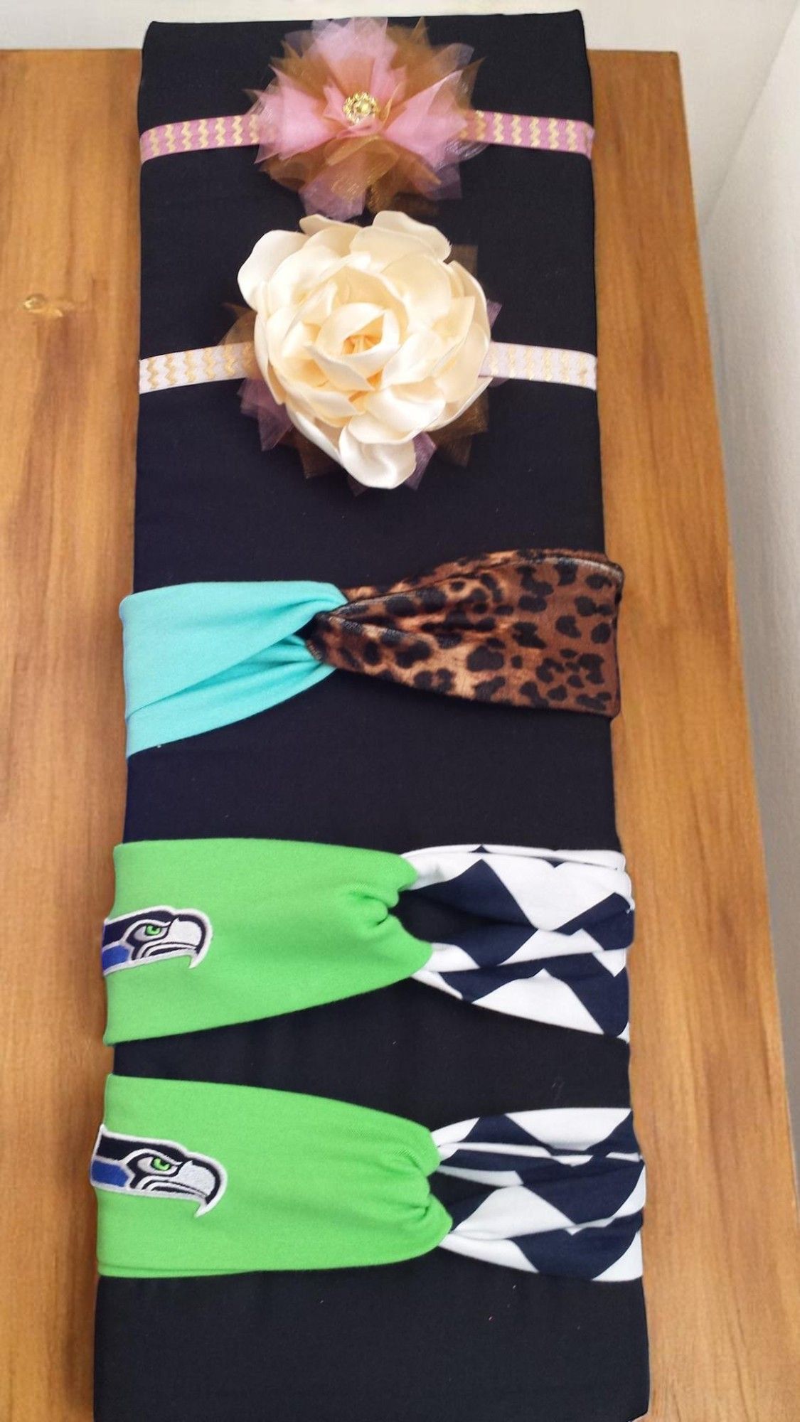 A dark fabric roll displays five headbands: two floral, one leopard print with teal, and two Seattle Seahawks themed.