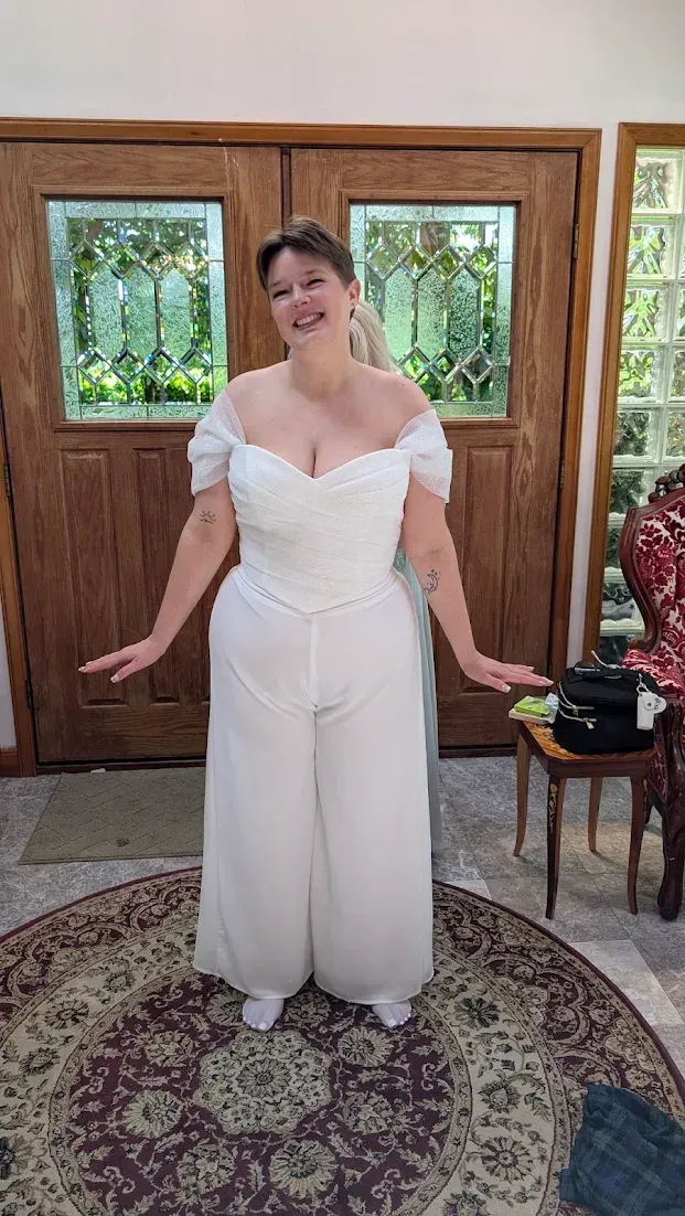 Woman in a white dress posing indoors in front of wooden doors and greenery.