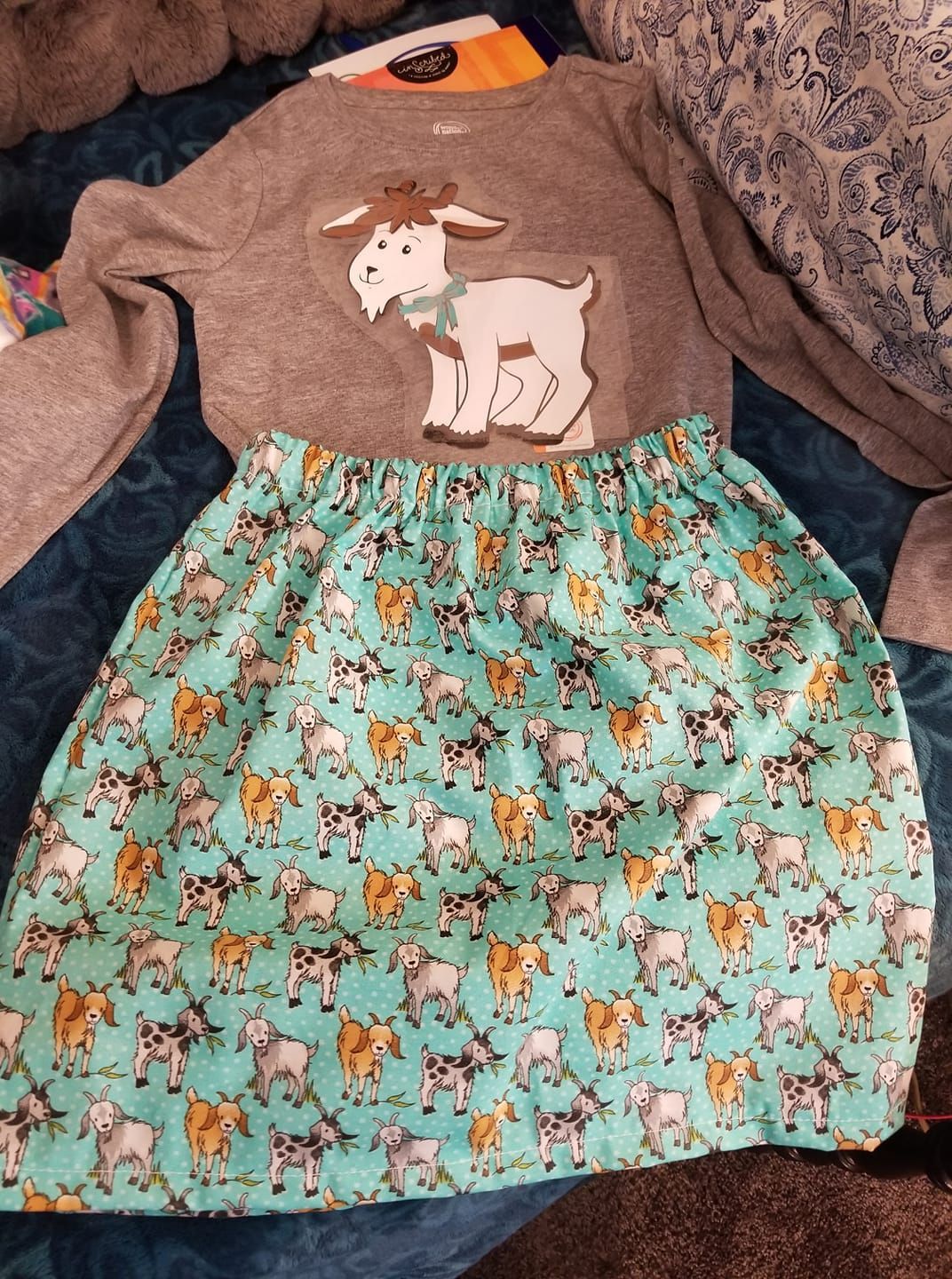 A long-sleeved gray shirt with a large goat appliqué, paired with a teal skirt featuring a repeating goat pattern.