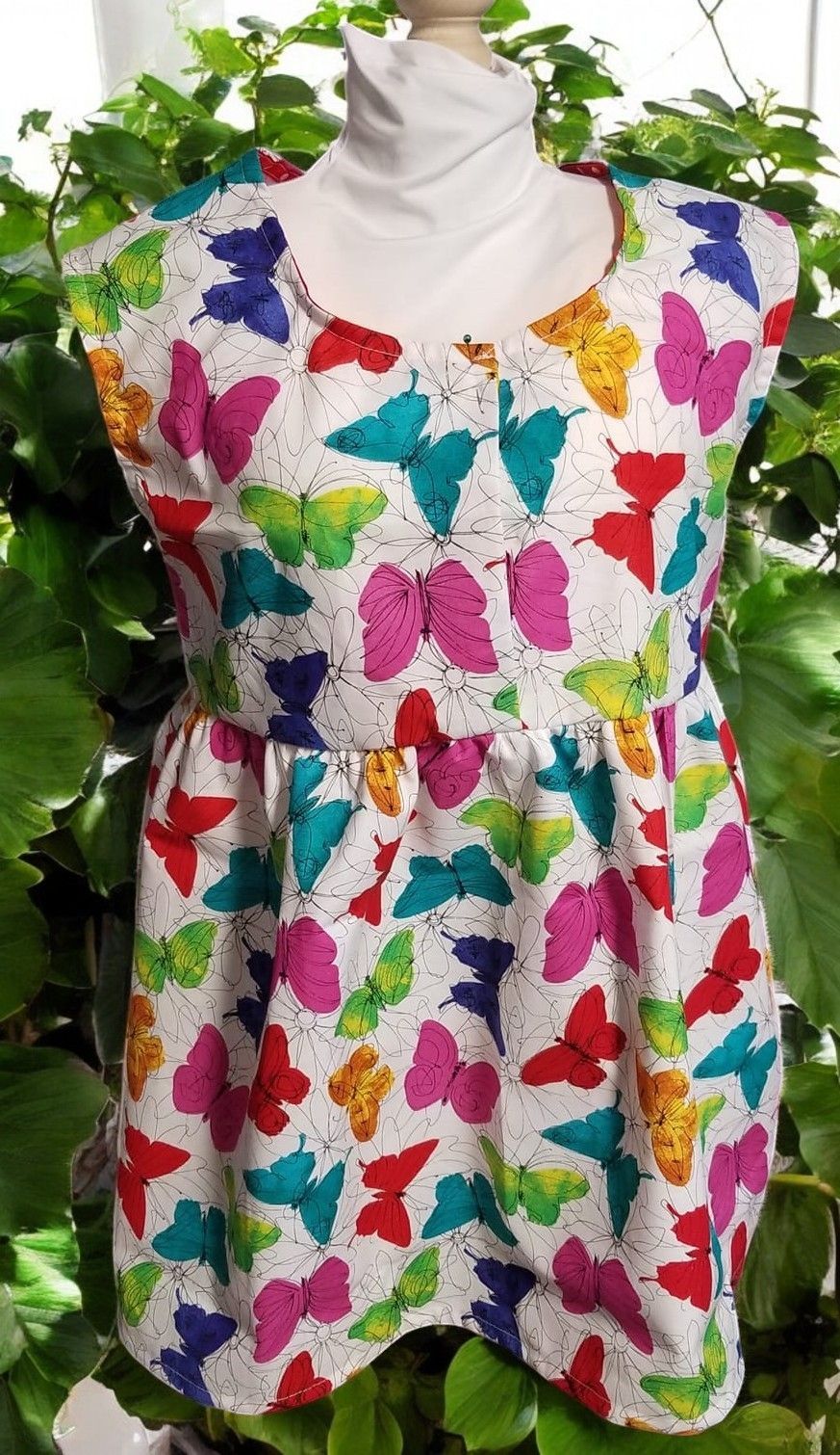 A sleeveless dress featuring a colorful pattern of butterflies in shades of blue, pink, red, and yellow on a white background.